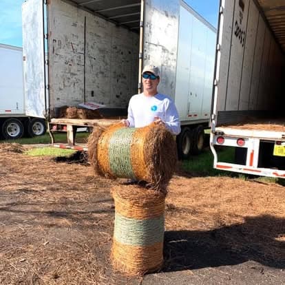 Richard standing with stacked pine straw bales between two semi trailers at the Fairhope yard