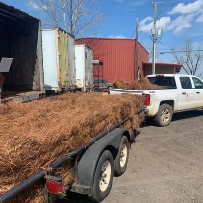 White pickup truck pulling a trailer loaded with fresh pine straw bales for delivery