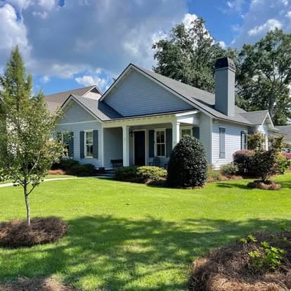 White-siding Fairhope home with fresh pine straw and shrubs along the foundation