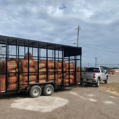 Large black trailer with cages full of pine straw bales next to a white pickup