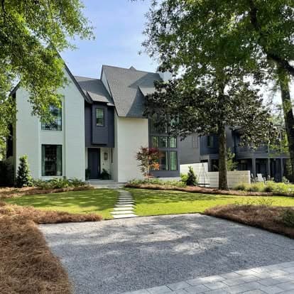 Modern white-and-dark farmhouse with stone walkway and fresh pine straw beds
